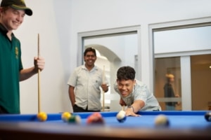 Photo of three boarding school students playing a game of pool in their recreation area