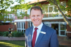 Mr Rod Steer, Head of Boarding smiling and looking into camera in a blue suit with red tie